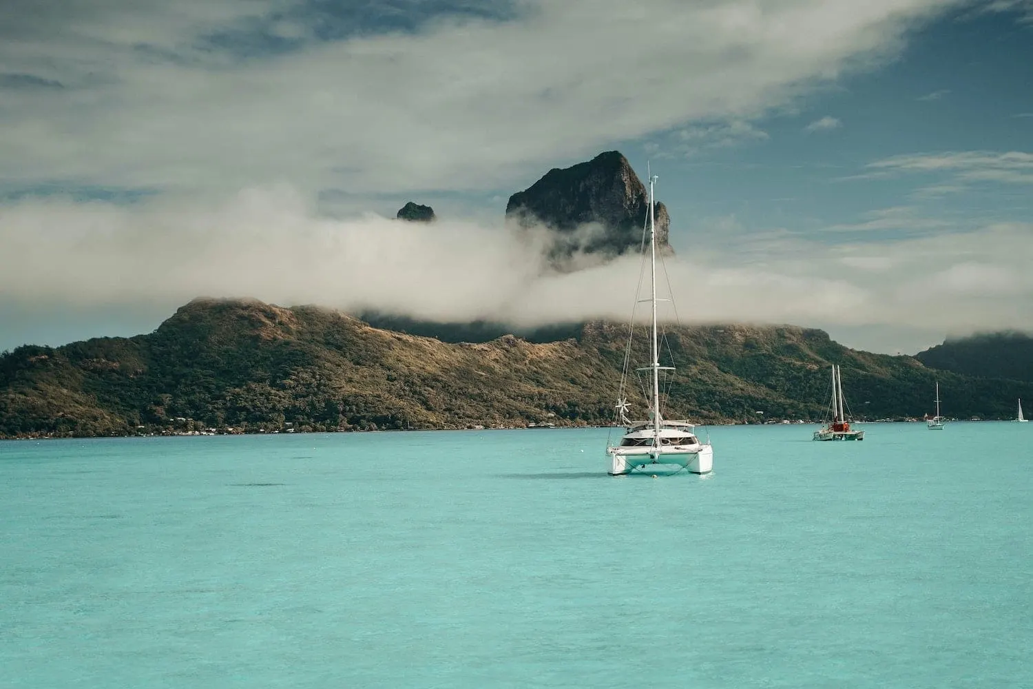 Catamaran at anchor in a turquoise lagoon off Bora Bora's peak