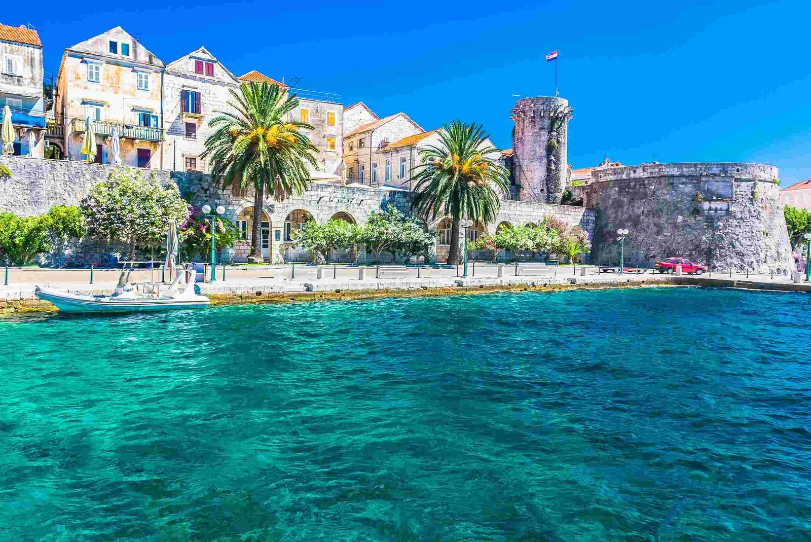 Korčula waterfront with stone walls and palms, small boat in clear water