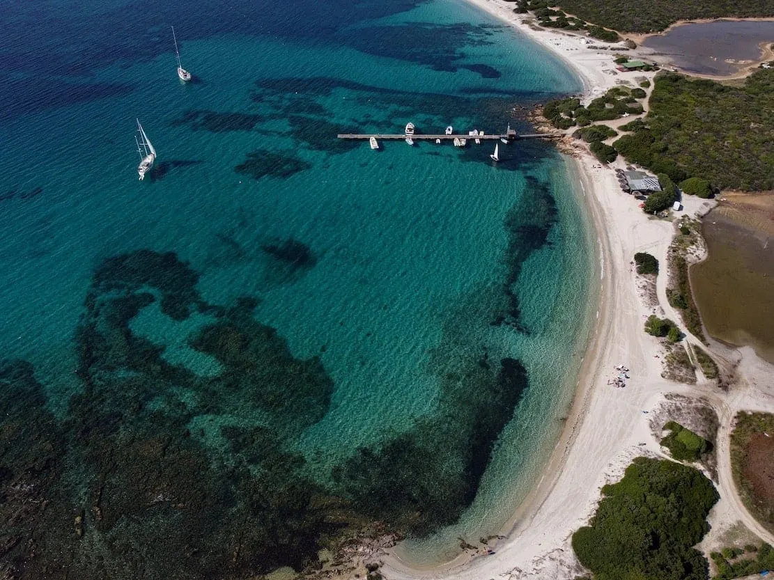 Aerial view of a white sand beach and clear bay with yachts at anchor