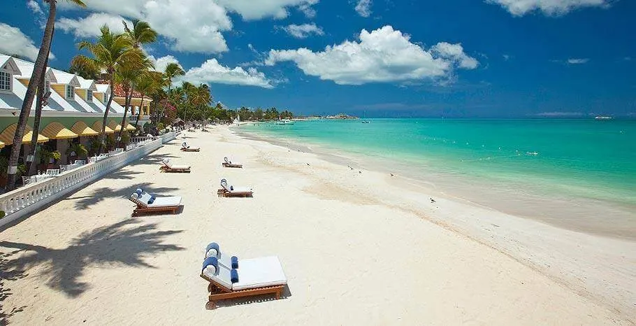 Moored boats rest on white sand beach with turquoise water and palm-lined shore in Caribbean location