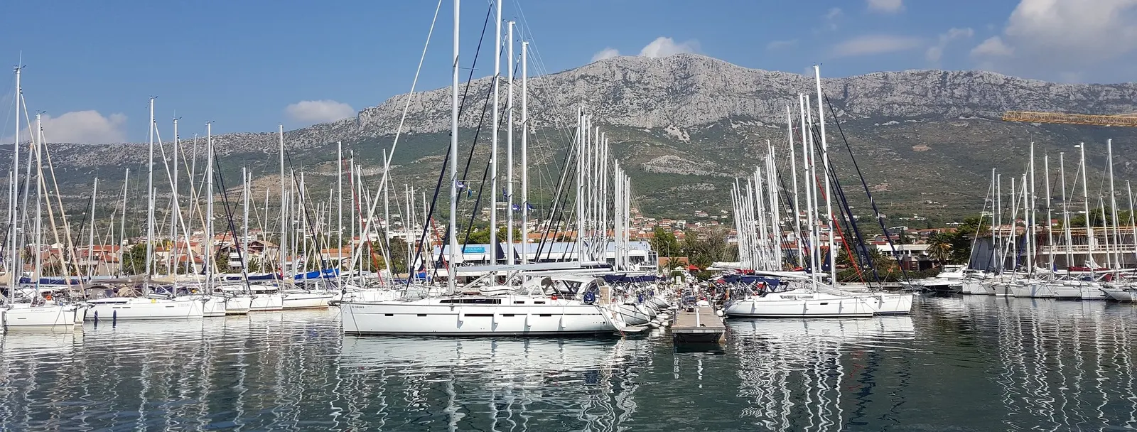 Rows of charter yachts moored in a Croatian marina below a limestone mountain